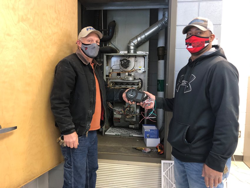From left to right: Terry Watkins and Tywon Davis install an iWave-R Residential Air Cleaner to help prevent COVID-19 in the Philadelphia Public School District.