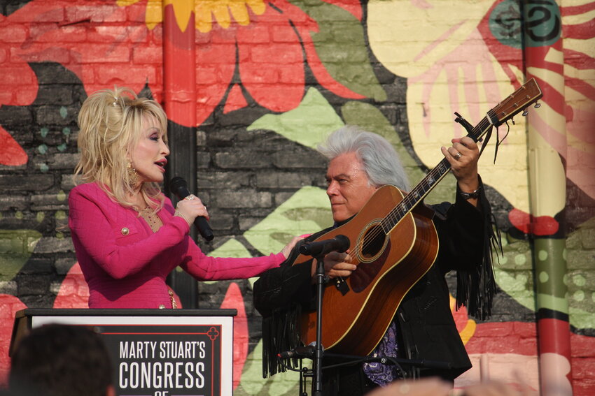 Country music icon Dolly Parton sings as Marty Stuart strums his guitar during the unveiling of a new downtown mural form a show this summer at the Ellis.